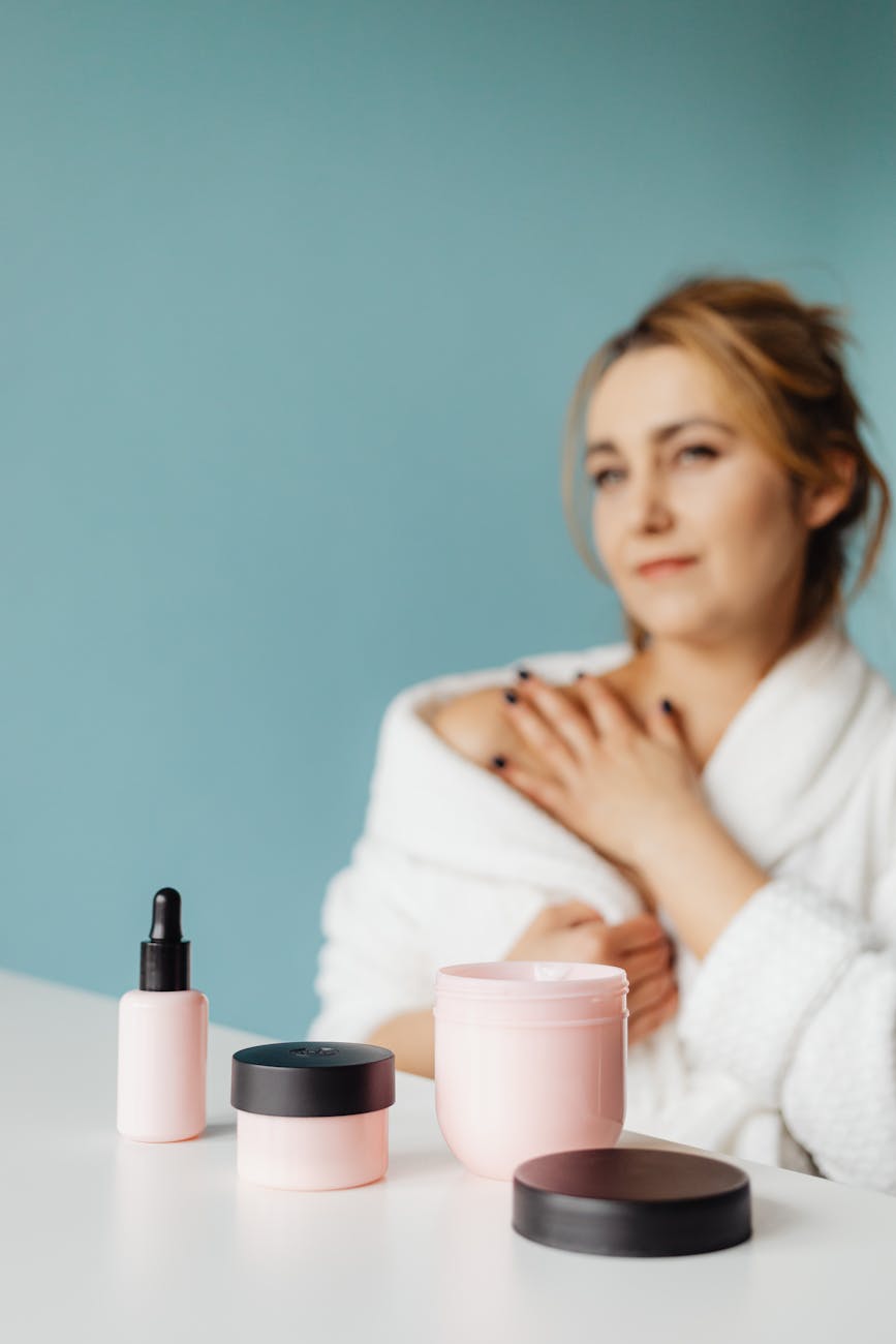 woman sitting in a bathrobe with beauty products in front of her on a table